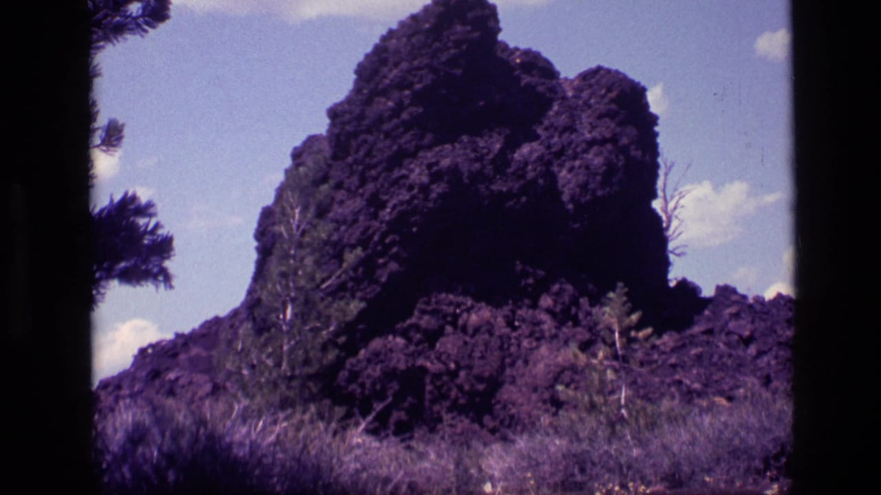 Jagged dark rock formation beside dry grass under a blue sky with scattered clouds.