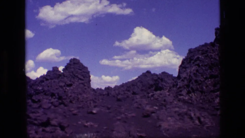 1972 Idaho 8mm frame looking across low jagged rock ridges, scattered stones, and a broad blue sky with puffy clouds.