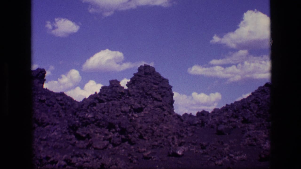 Jagged dark volcanic rocks beneath a blue sky with scattered clouds.