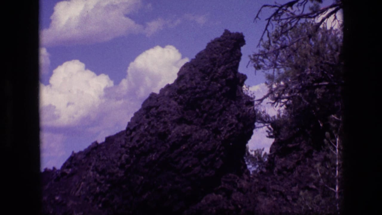 1972 Idaho 8mm frame with the rock formation closer in view, bordered by branches and set against puffy clouds.