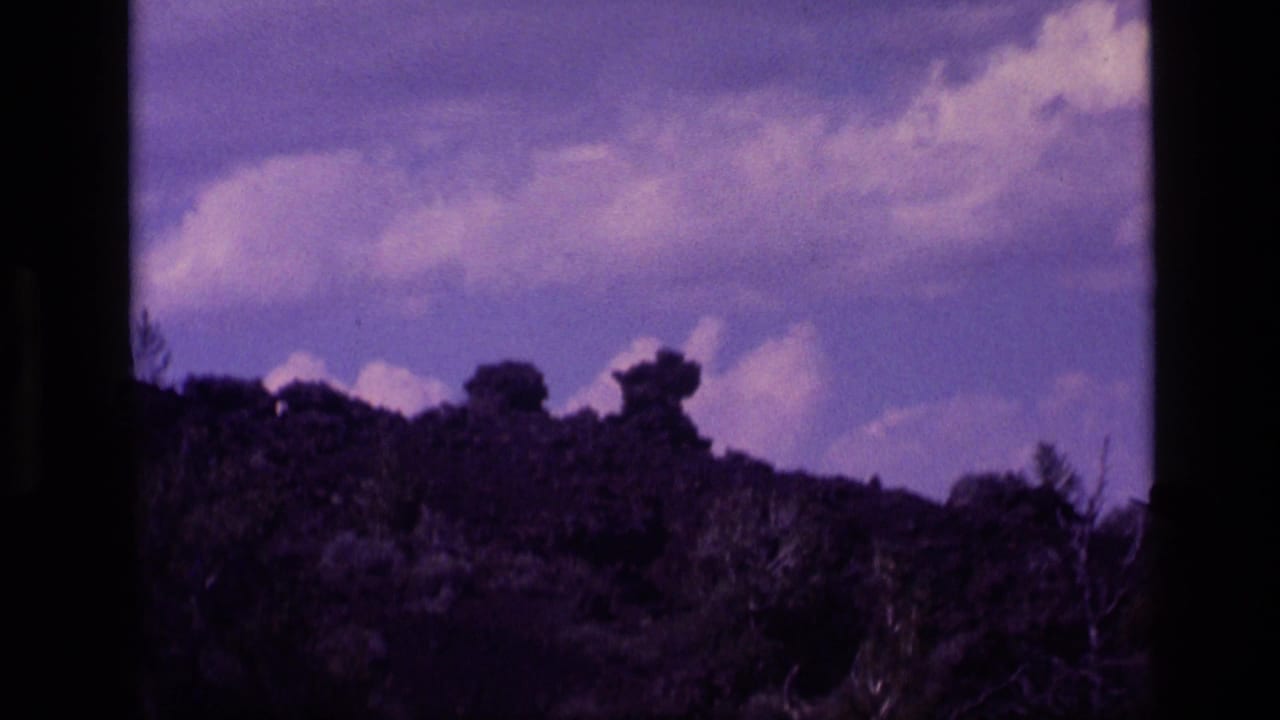 Purple-tinted hillside silhouette beneath a cloudy sky, bordered by dark vertical frame edges.