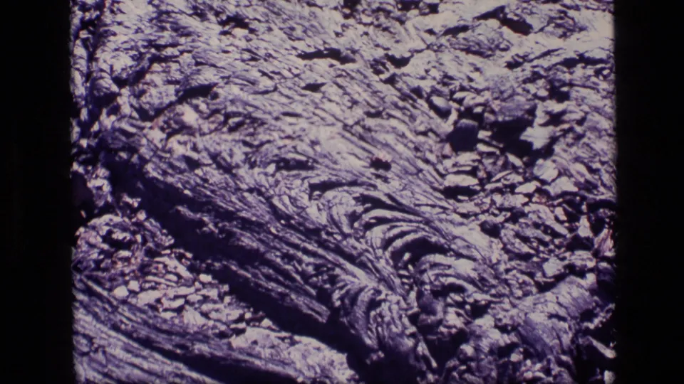 1972 Idaho 8mm close-up of rough organic texture, with diagonal ridges, dark recesses, and small broken surface pieces.
