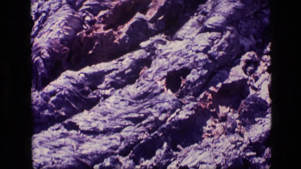Aged 8mm frame from Idaho showing layered rock ledges, small cavities, and dry debris across an uneven surface.