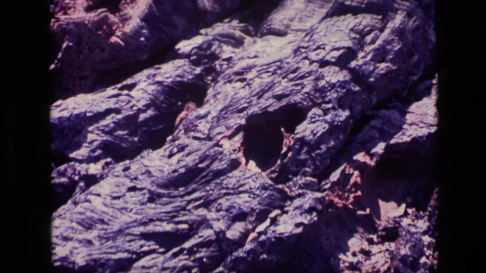 1972 Idaho 8mm close-up of a weathered rock face marked by dark holes, ridged stone, and broken fragments.
