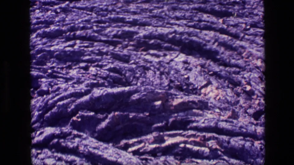 1972 Idaho 8mm frame showing a close-up of rough, ropy cooled lava flow with purple color shift and film grain.