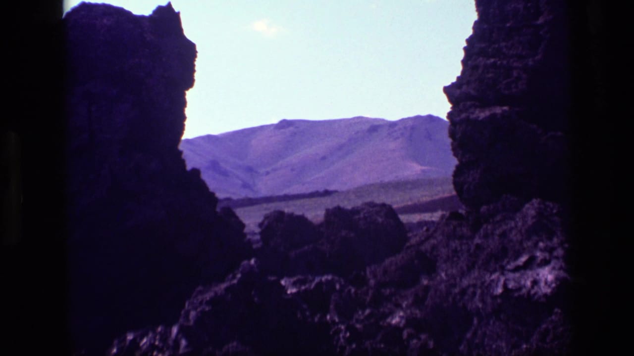 1972 Idaho 8mm frame showing silhouetted rocky formations with mountain ridges beyond and a bright sky overhead.