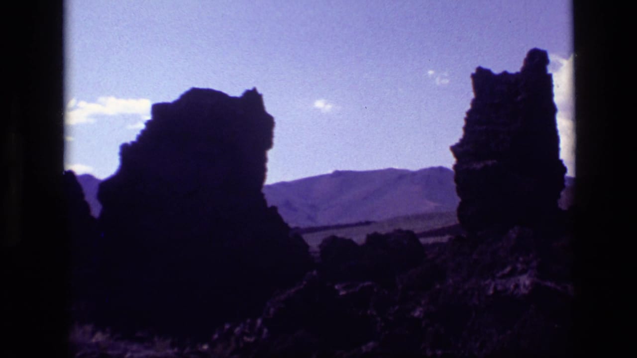 Silhouetted rock spires stand before low mountain ridges and scattered clouds.