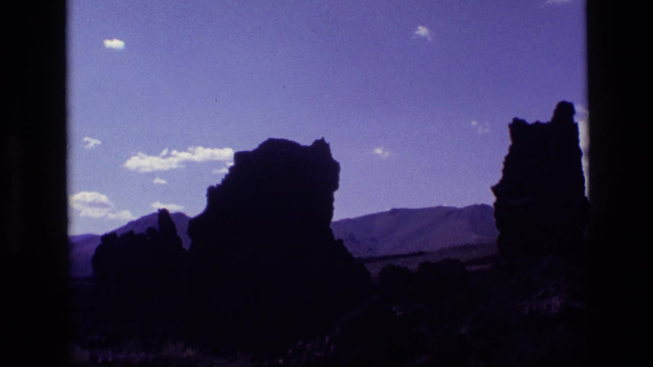 Dark rock formations silhouetted against a blue-purple sky with clouds and distant hills.