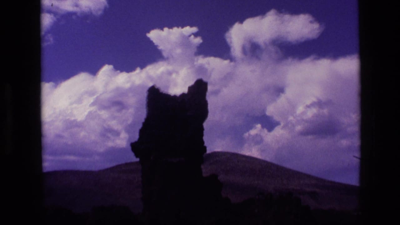 Single dark rock spire below large white clouds and a saturated blue sky.