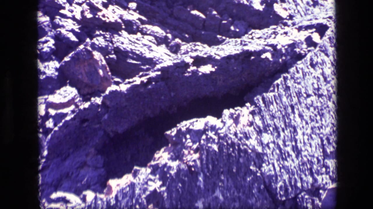 Close view of rough, purple-hued rock with strong sunlit highlights.