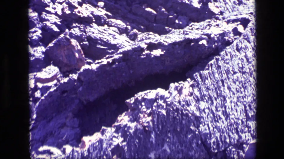 Close 1972 Idaho 8mm view of rough rock surfaces with bright highlights, deep shadows, and a pronounced purple color shift from the film scan.