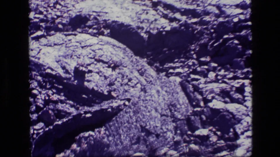 Final 1972 Idaho home-movie frame showing uneven rocky ground, jagged stones, and strong purple-tinted contrast across the terrain.