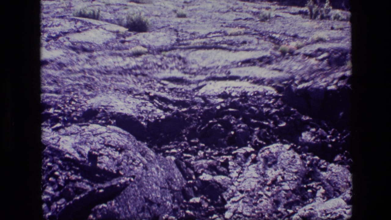 1972 Idaho 8mm view of close, uneven rock surfaces with scattered boulders and sparse scrub.
