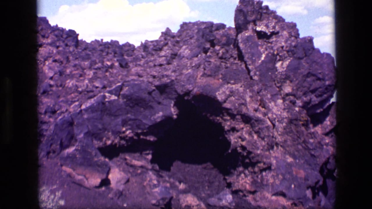 1972 Idaho 8mm frame showing a rough rocky hillside and dark cave-like entrance with aged purple color shift.