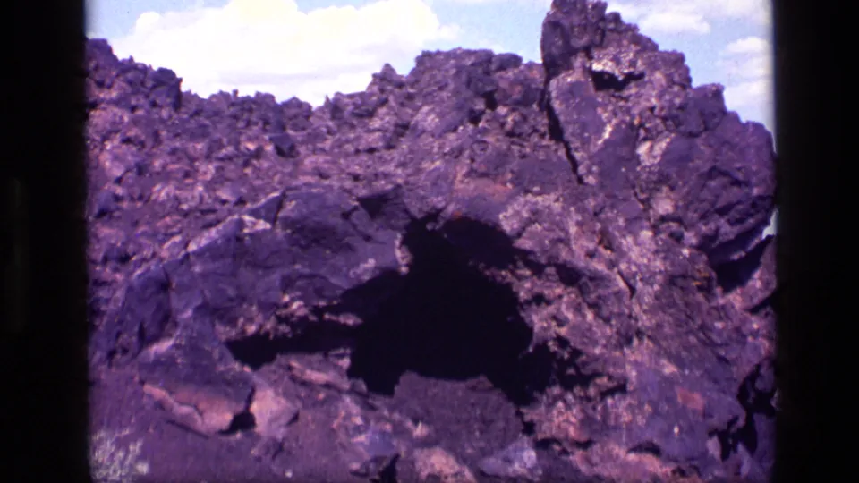 1972 Idaho 8mm frame showing a rough rocky hillside and dark cave-like entrance with aged purple color shift.
