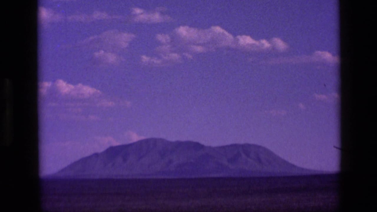 1972 Idaho 8mm frame with a distant mountain form across a low horizon beneath a purple-tinged sky.