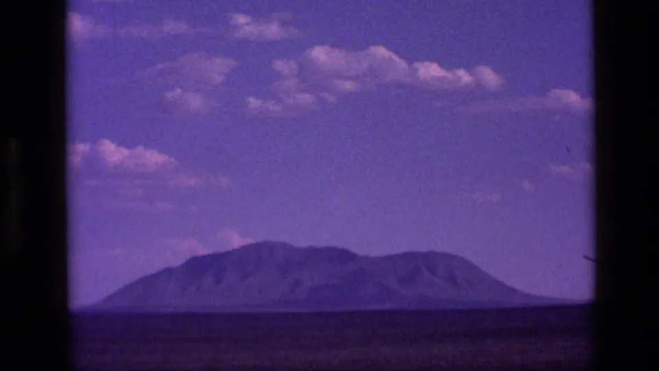 1972 Idaho 8mm frame with a distant mountain form across a low horizon beneath a purple-tinged sky.