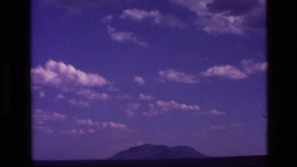 1972 Idaho 8mm frame holding on a distant mountain beneath a clouded, purple-toned sky.
