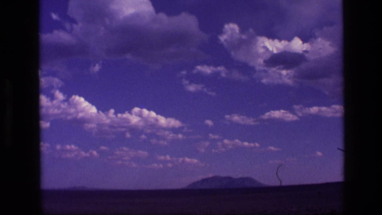 1972 Idaho 8mm frame with cumulus clouds above a flat open landscape and distant mountain silhouette.