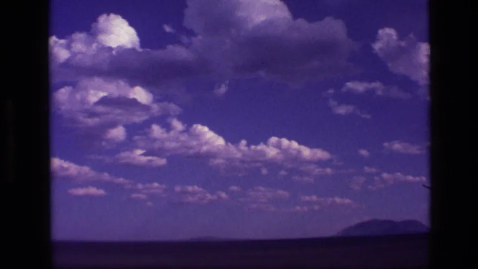 1972 Idaho 8mm frame showing large cumulus clouds over open terrain with a distant mountain near the horizon.