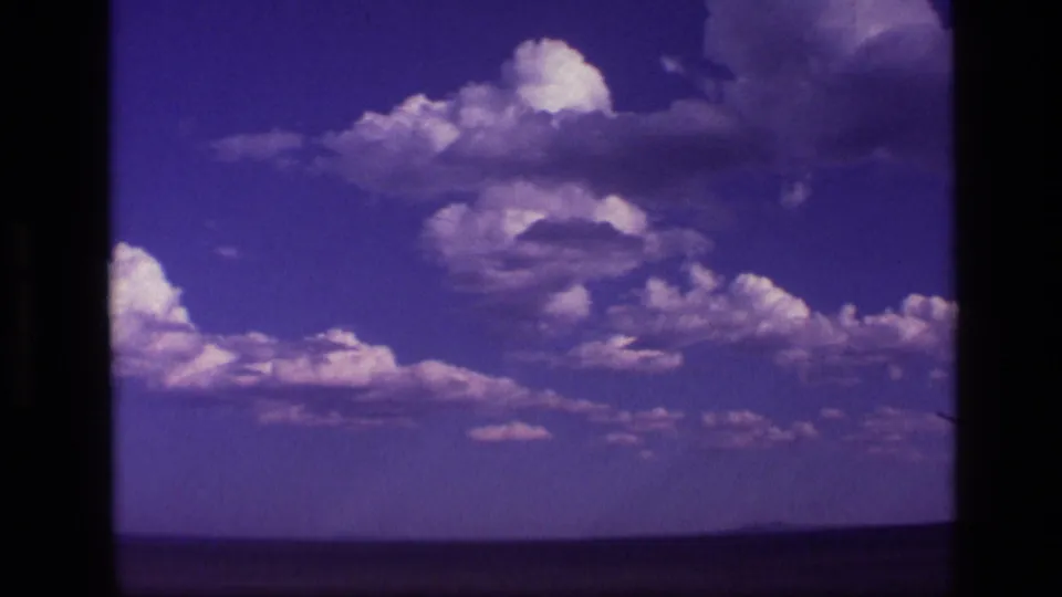 1972 Idaho 8mm frame of bright cumulus clouds over a flat western landscape with distant mountains at the horizon.