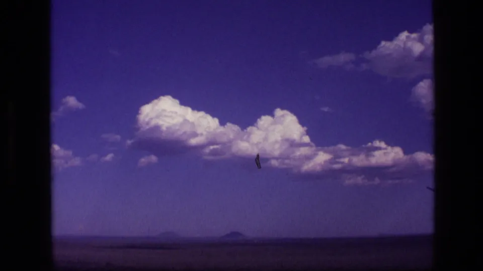 1972 Idaho travel footage frame with bright clouds, open plain, and faint mountain silhouettes along the horizon.