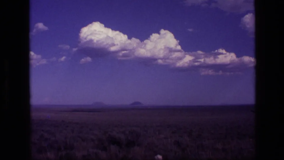 1972 Idaho 8mm frame showing scrubby foreground, low horizon, clustered clouds, and distant landforms.