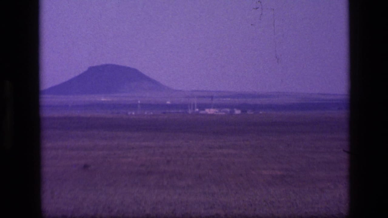 1972 Idaho 8mm frame showing an arid grassland, low horizon, and distant mountain beneath a magenta-purple sky.