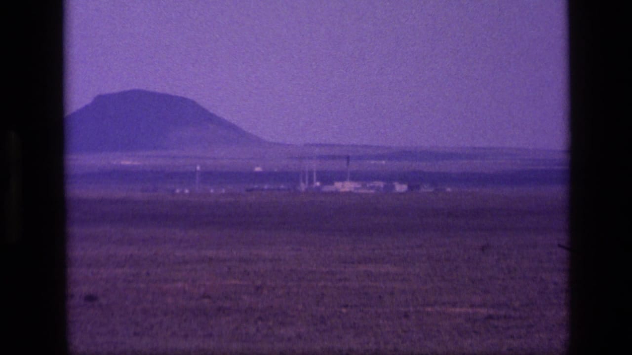 1972 Idaho 8mm frame with a distant mountain, open dry plain, and small far-off structures near the horizon.
