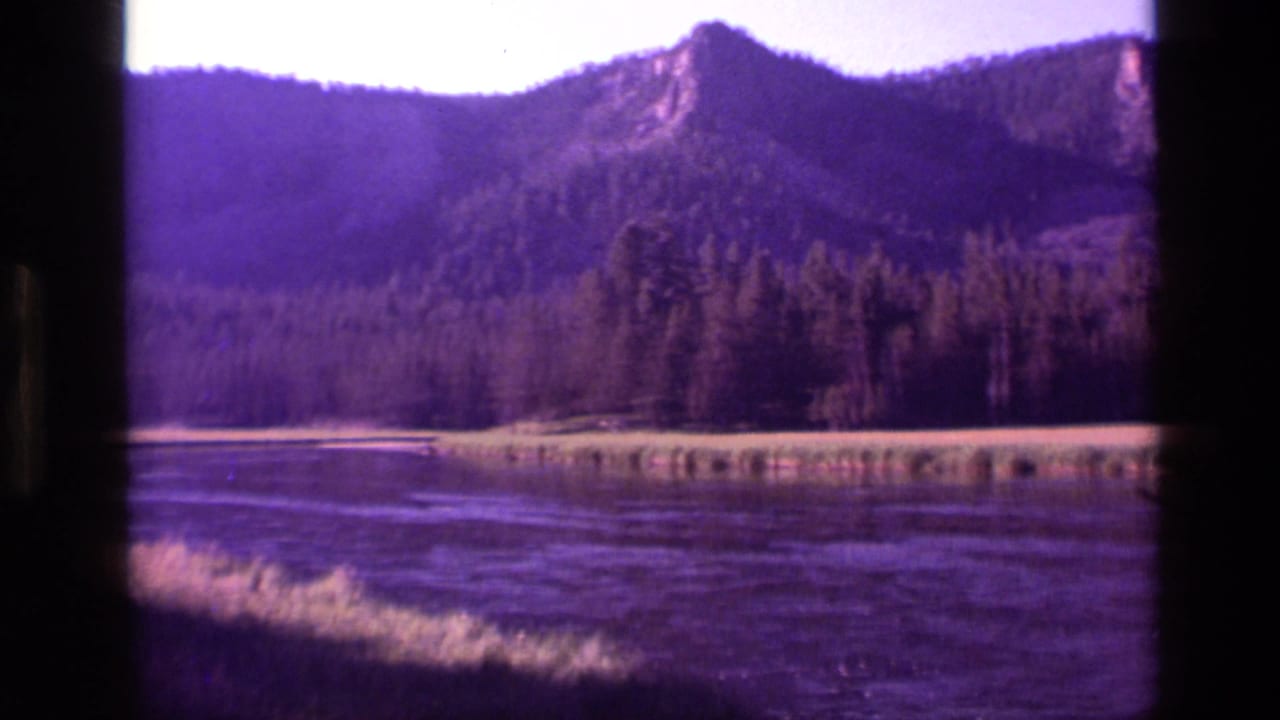 Forested mountain ridge above a calm body of water with dark film-gate borders.