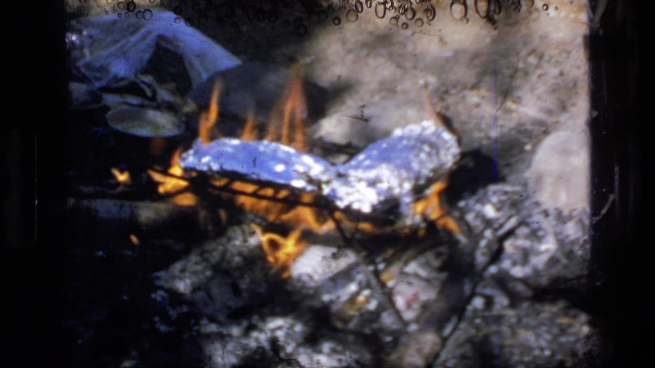 Foil-wrapped food cooking in flames among ash and rocks.