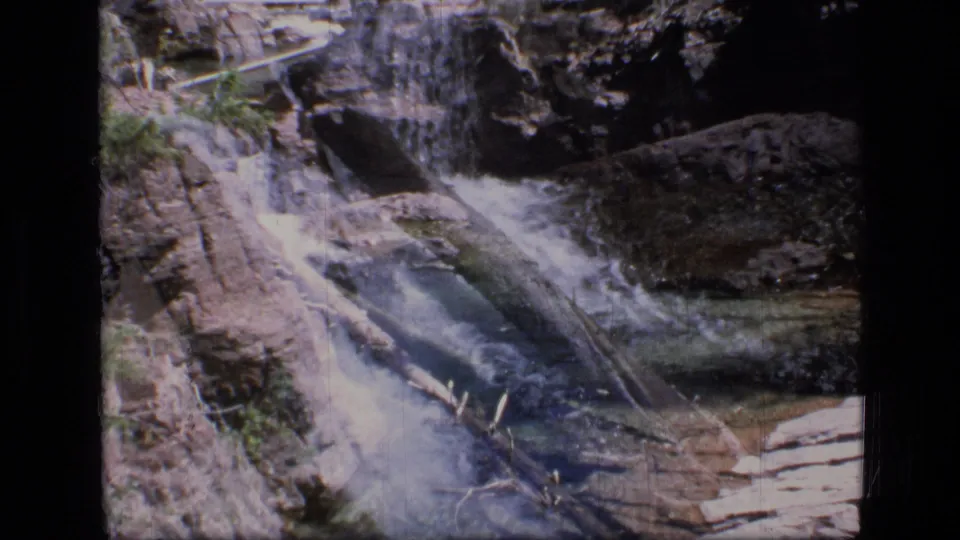 1973 Scapegoat Wilderness frame showing water descending through rocks toward a darker pool, with downed wood in the channel.