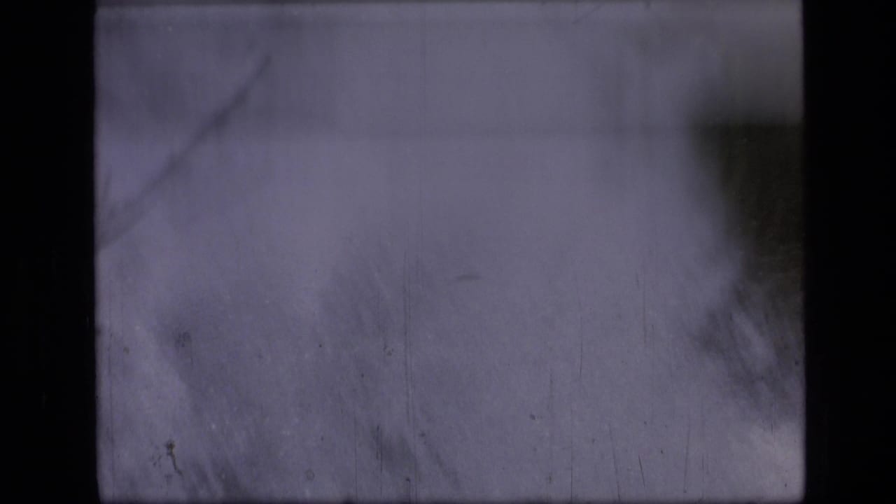 Opening 1973 8mm frame from the Montana wilderness clip, mostly obscured by darkness with a soft pale patch and visible film wear.