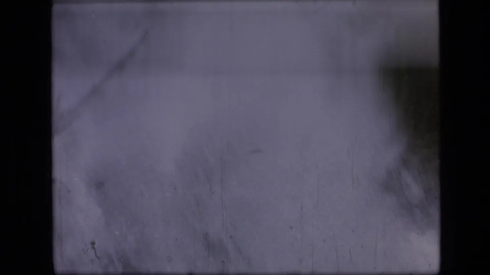 Opening 1973 8mm frame from the Montana wilderness clip, mostly obscured by darkness with a soft pale patch and visible film wear.