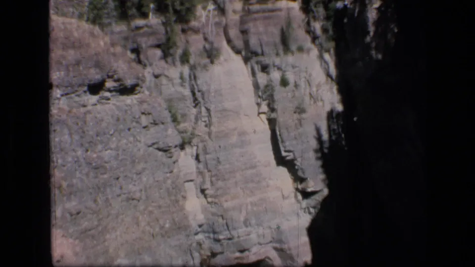 Scapegoat Wilderness canyon wall in 1973 8mm footage, showing layered rock, cliff shadows, and scattered evergreens.