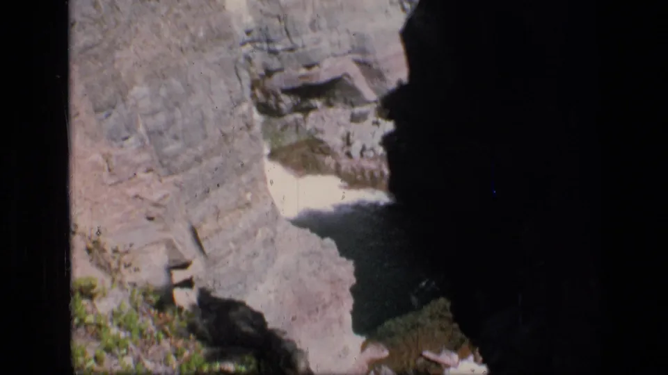 End frame of the 1973 Scapegoat Wilderness clip, with a shadowed ravine, sheer rock faces, and pale water below.
