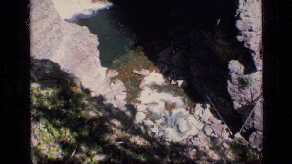 A high-angle 8mm frame from Scapegoat Wilderness shows steep rock, a small dark pool, and strong contrast between sun and shade.