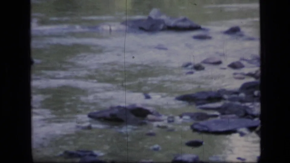1973 Montana wilderness home-movie frame showing rippling water and rounded rocks in a softly exposed 8mm scan.