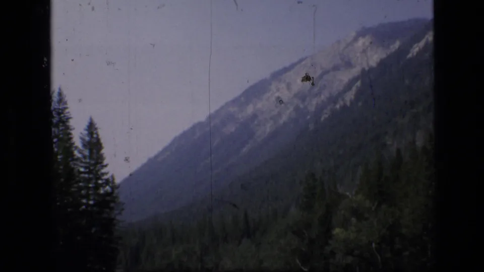 Scapegoat Wilderness mountain vista on 1973 8mm film, with forested slopes, pale sky, and visible film scratches.