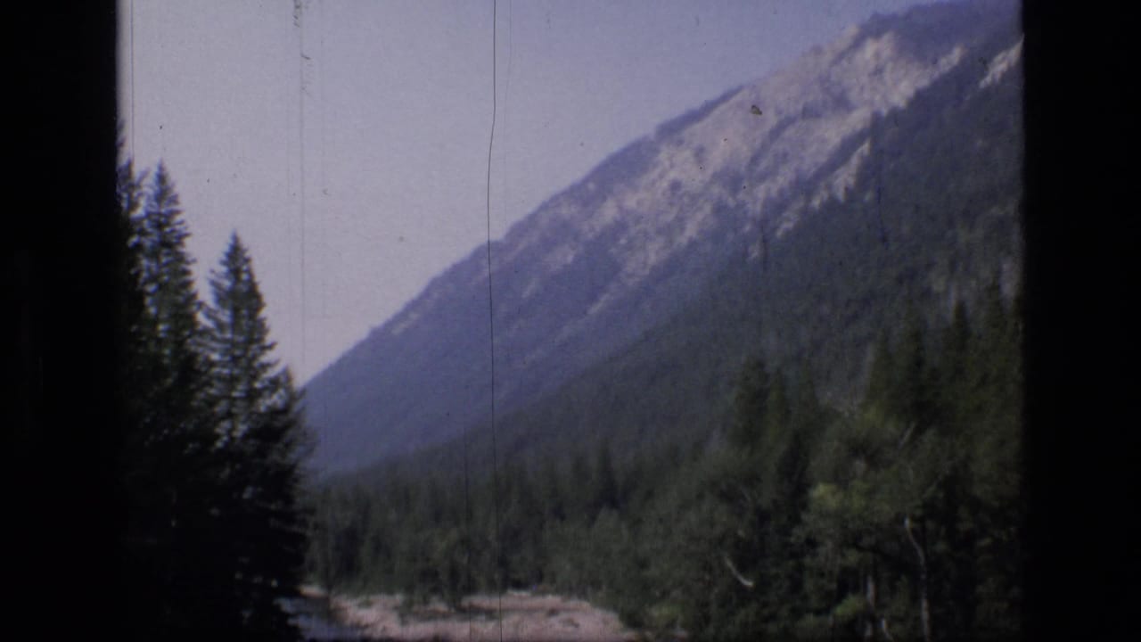 Forested mountain slope above a river valley with dark film-frame borders.