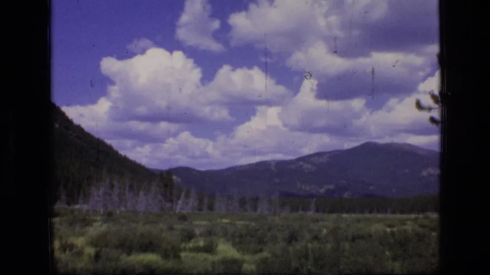 Scapegoat Wilderness landscape on 8mm film, showing meadow, forest, mountains, and a bright clouded sky.