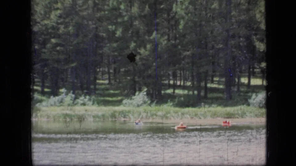 1973 8mm view of people swimming and floating near shore on a forested lake in Scapegoat Wilderness, Montana.