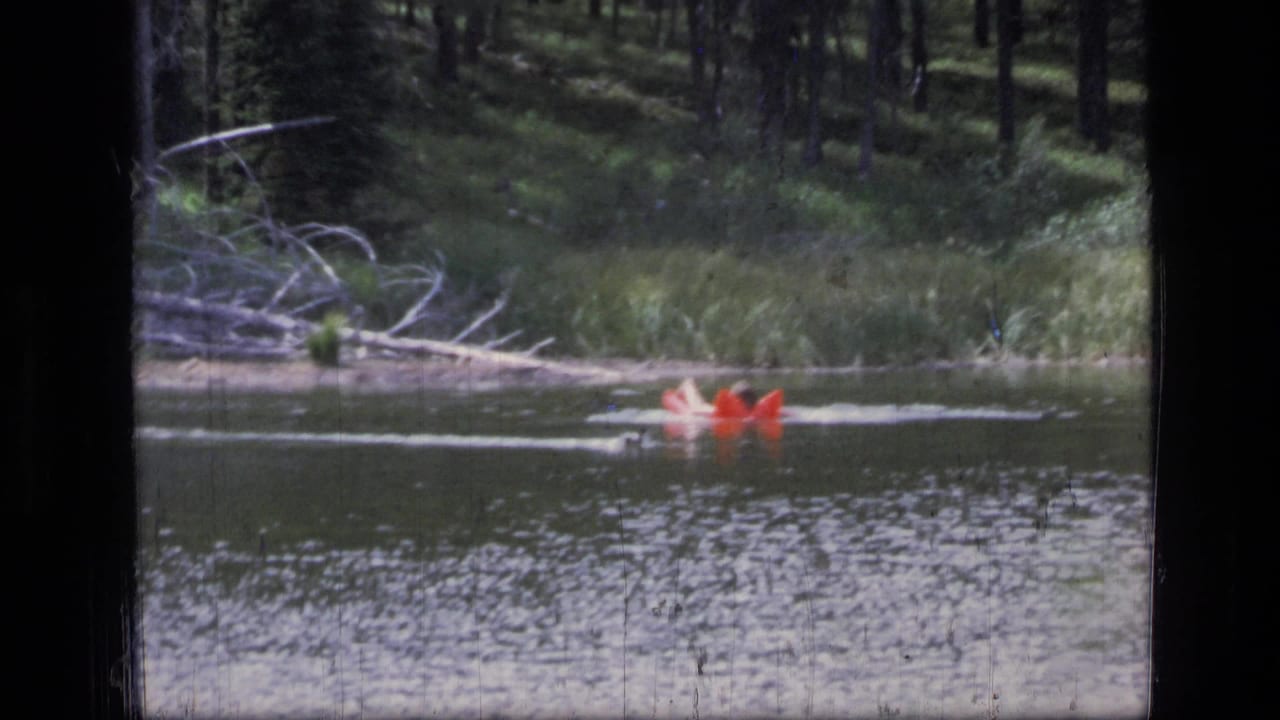 Red inflatable raft moving across a calm lake near a forested shore.