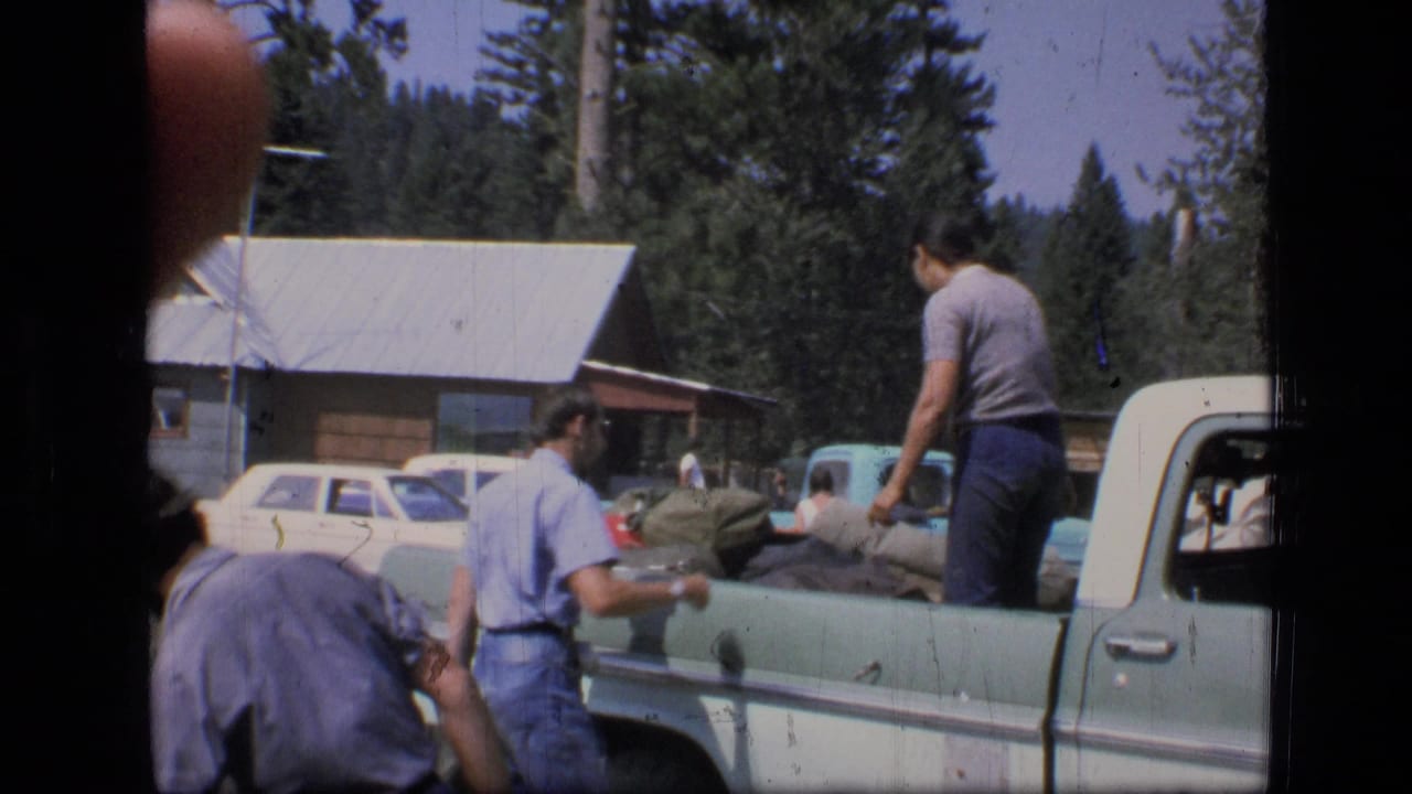 1973 Montana home-movie frame showing people unloading bags from a two-tone pickup in a rural mountain setting.