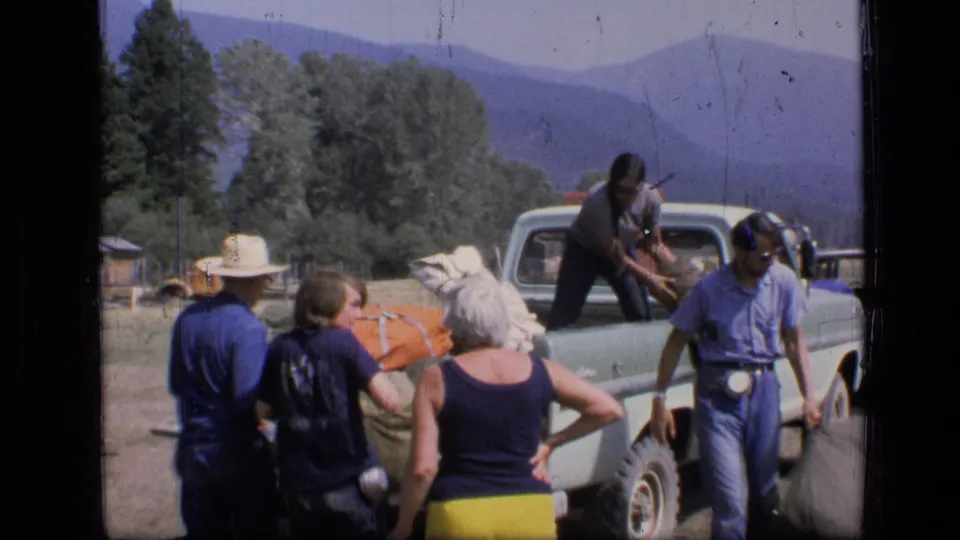 Adults in casual clothes stand by a loaded pickup in the Scapegoat Wilderness area, with trees and mountains behind them.