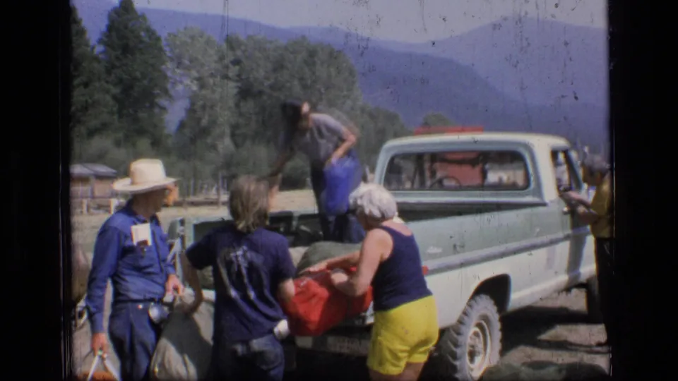 Adults in summer clothing load or unload camping bags beside a light pickup in Scapegoat Wilderness, Montana, 1973.