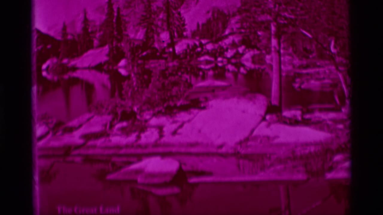Magenta forested lake view with rocks, shoreline, water, and a picnic table near the foreground.