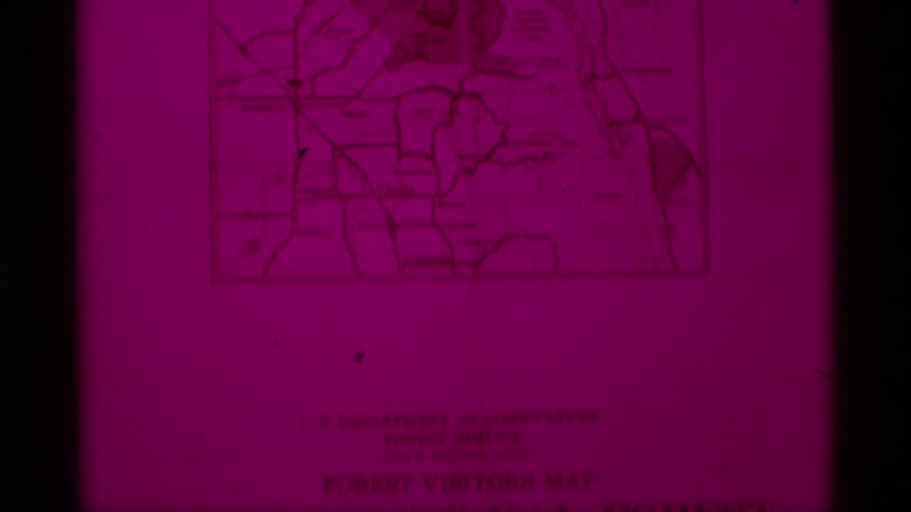 1975 8mm frame showing a magenta-tinted close-up of a Sierra National Forest visitors map with faint labels and border lines.