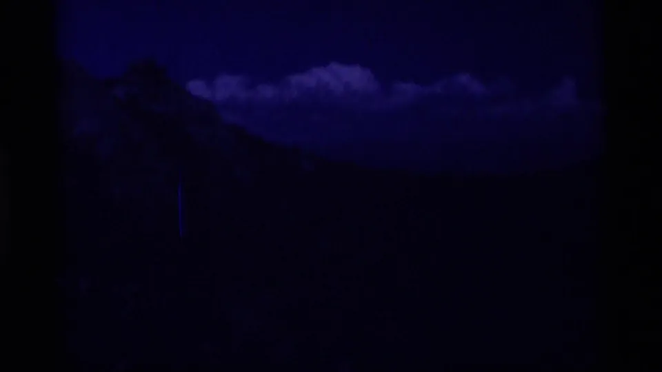 Underexposed 8mm view of a forested mountain valley beneath cloud cover, likely part of the Minaret Wilderness sequence.