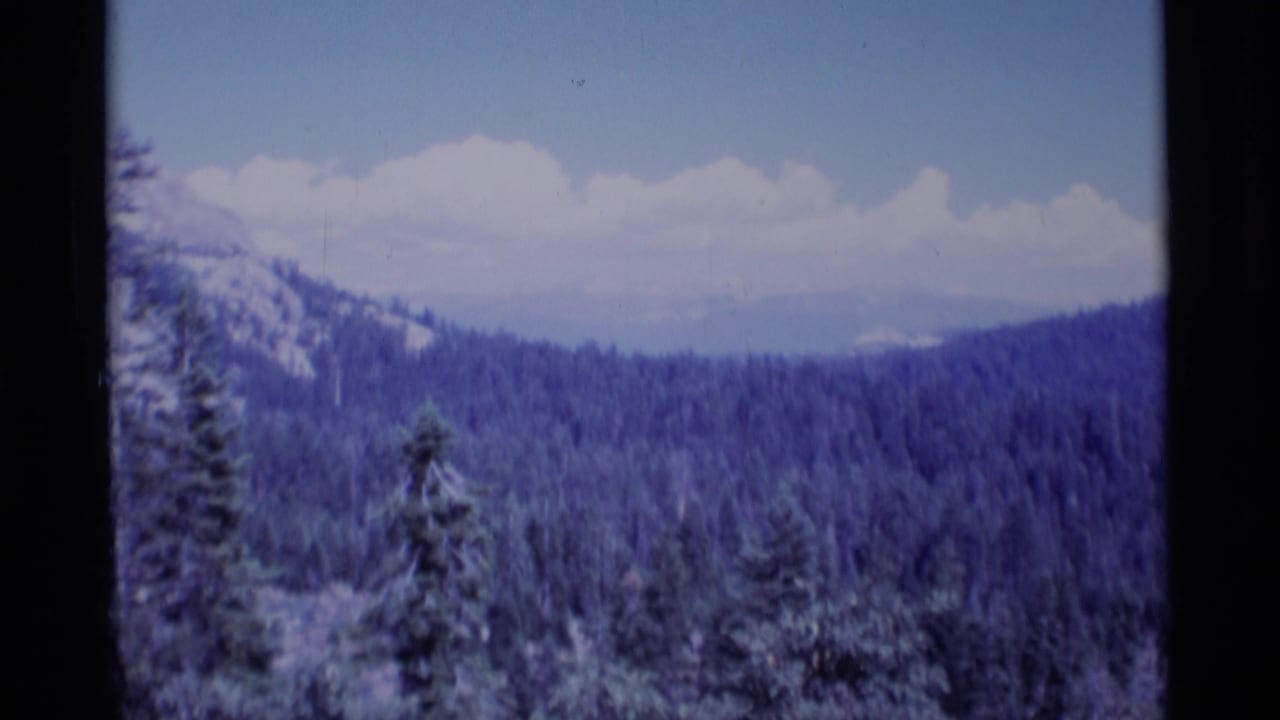 Evergreen-covered hills and distant mountains under a band of white clouds.